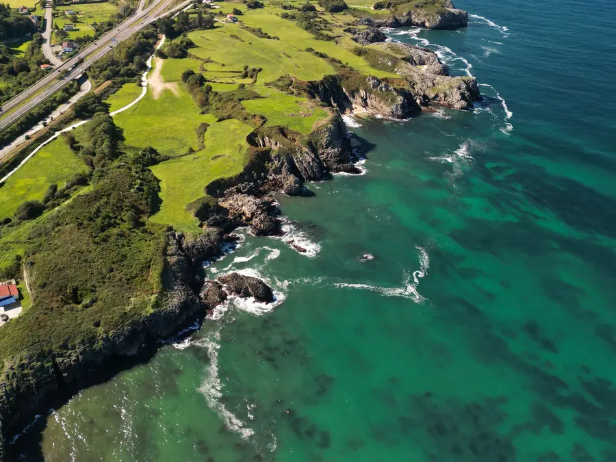 The Asturian coast seen from the air: green fields ending in dark cliffs and clear turquoise water.