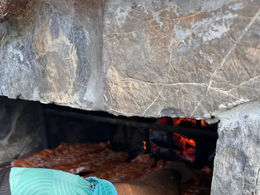 Meat on a grill inside a stone hearth, with the fire glowing behind it.