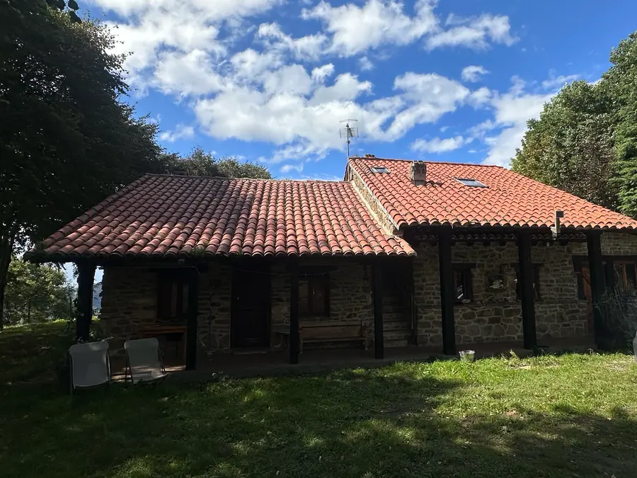A stone house with a red tiled roof and a covered porch, under a blue sky with scattered cloud.